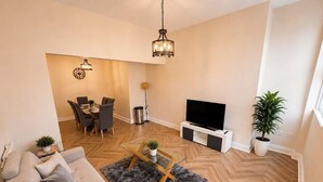 A modern living room with a sofa, coffee table, TV stand, and dining area.