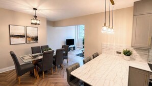 A modern kitchen with a marble countertop, a dining area with a glass table, and a TV in the background.