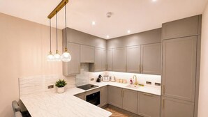 A modern kitchen with marble countertops, grey cabinets, and a herringbone wood floor.