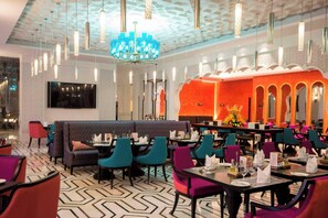 Un restaurant au décor moderne, avec un sol à motifs, différents types de sièges, notamment des banquettes et des tables, et un lustre central.