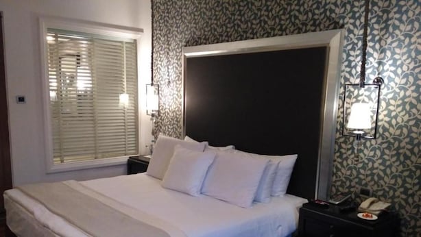Un letto rifatto con lenzuola e cuscini bianchi, un comodino con una lampada e una carta da parati decorata.