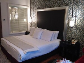 A neatly made bed with white linens and pillows, a bedside table with a lamp, and a patterned wallpaper. - Itc Rajputana A Luxury Collection Hotel (Jaipur)