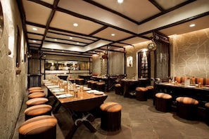 A restaurant with long communal tables, cushioned stools, and a stone wall. - Itc Rajputana A Luxury Collection Hotel (Jaipur)