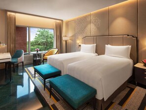 A hotel room with two beds, a desk, a chair, and a view of greenery outside. - Itc Rajputana A Luxury Collection Hotel (Jaipur)