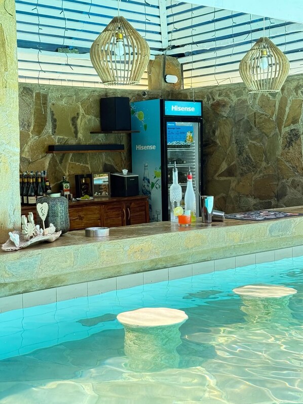 Zona de piscina con bar, paredes de piedra y lámparas colgantes.