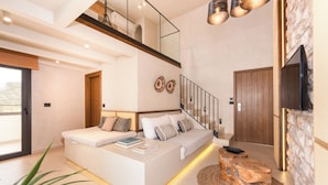 A modern bedroom with a large bed, a staircase, a TV, and a stone wall. - The Sand Suites (Agios Nikolaos)
