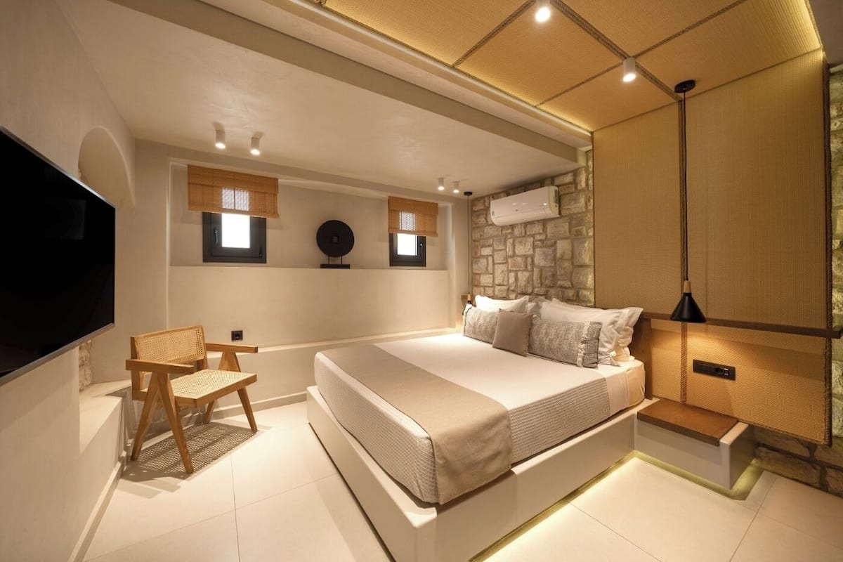 Ein modernes Schlafzimmer mit einem großen Bett, einem Fernseher, einem Sessel und einer Wand mit Steinverkleidung.