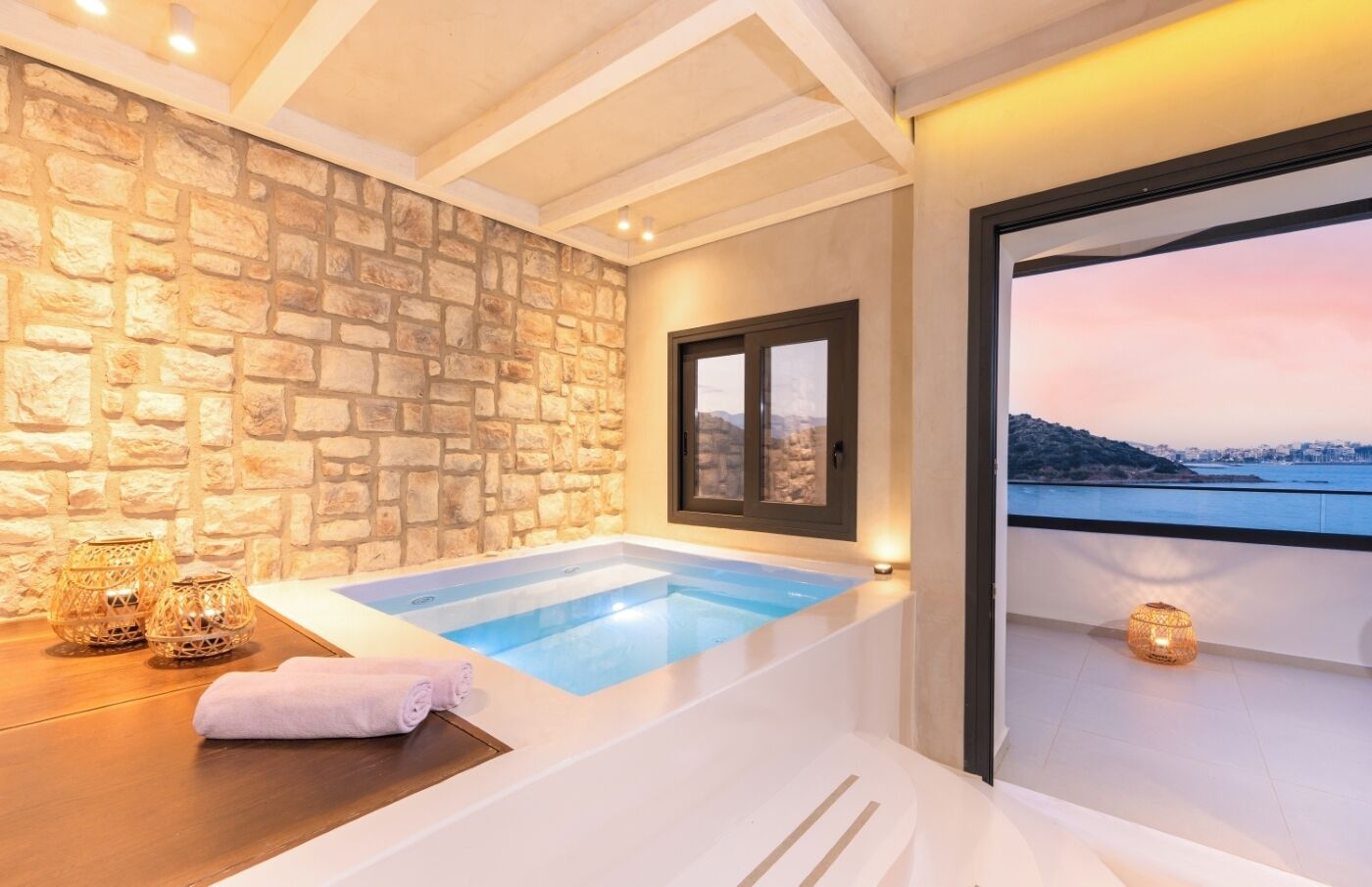 A spa area with a stone wall, a window, a bathtub, and a view of the sea.