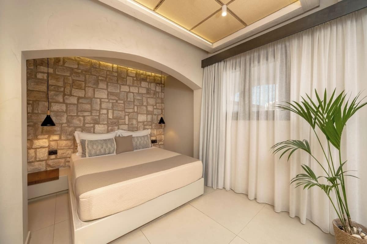 Ein Schlafzimmer mit Steinsandsteinwand, einem Bett, einem großen Fenster mit Vorhängen und einer Topfpflanze.