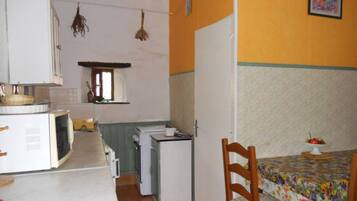A compact kitchen with a dining area, a microwave, a refrigerator, and a small table with a floral tablecloth.