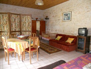 A room with a dining table, chairs, a sofa, a television, and a stone wall.