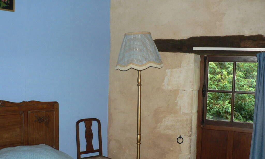 A room with a wooden bed, a chair, a floor lamp, and a window with a view of greenery.