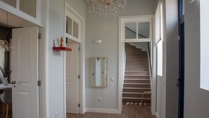 Un pasillo con una escalera, un candelabro y un espejo en la pared.