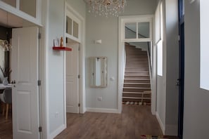 A hallway with a staircase, a chandelier, and a mirror on the wall.