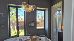 Comedor con una mesa redonda dispuesta para cuatro, sillas, una araña y vistas al exterior a través de amplios ventanales.
