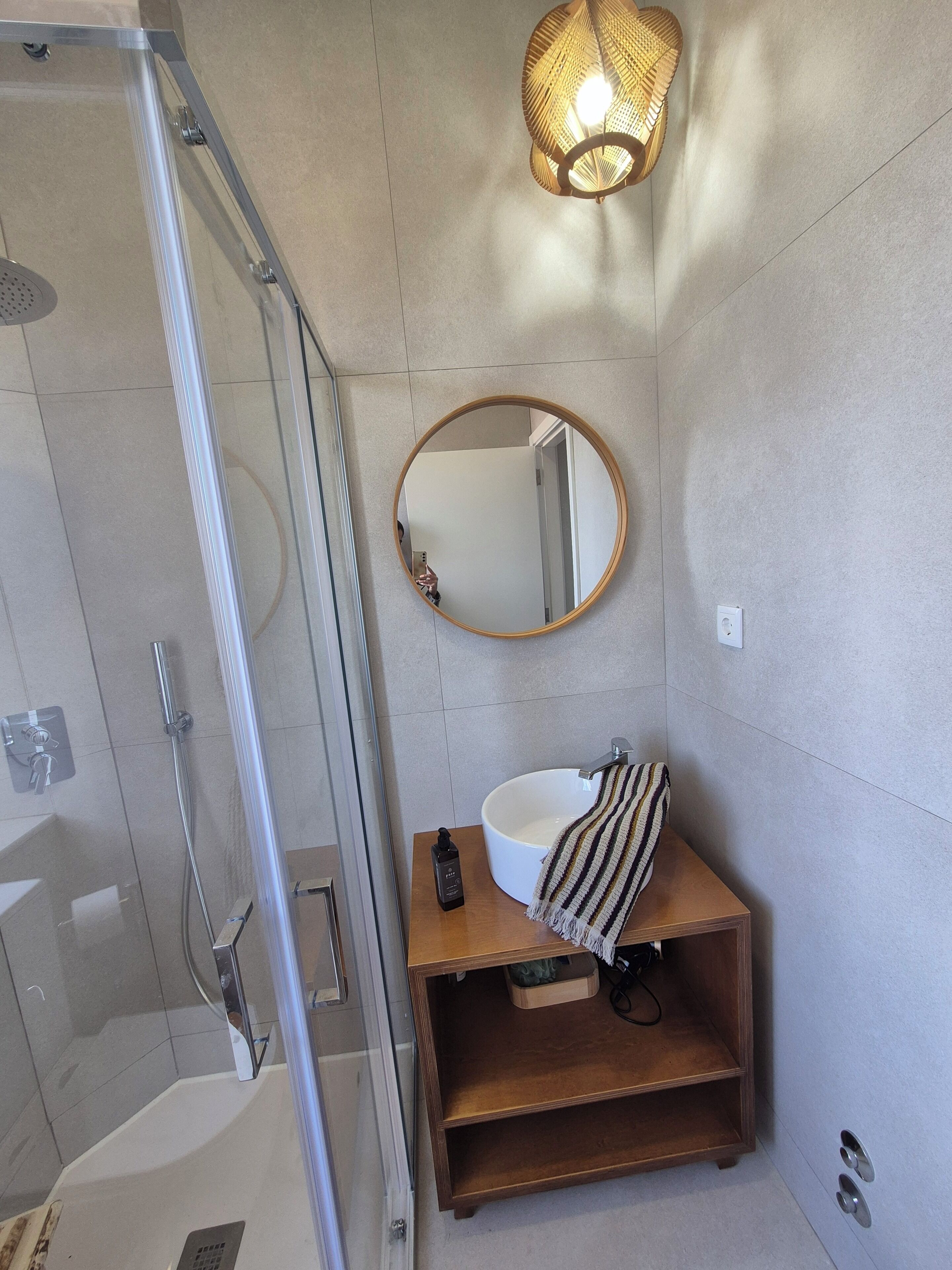 Un baño con cabina de ducha de vidrio, un espejo redondo, un lavabo blanco y un mueble de tocador de madera.