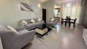 A living room with a grey sofa set, a black coffee table, and a dining area with a table and chairs. - Elite Apartments (Kigali)