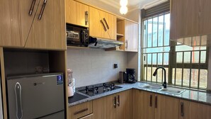 A modern kitchen with wooden cabinets, a built-in oven, a gas stove, and a window with a view. - Elite Apartments (Kigali)