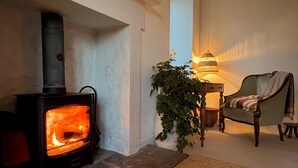 Ein gemütliches Zimmer mit Kaminofen, bequemen Sesseln, einer Lampe und einem Blumentopf.