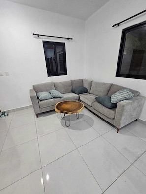 Ein modernes Wohnzimmer mit einem grauen Ecksofa, einem Holztisch und einem großen Fenster.
