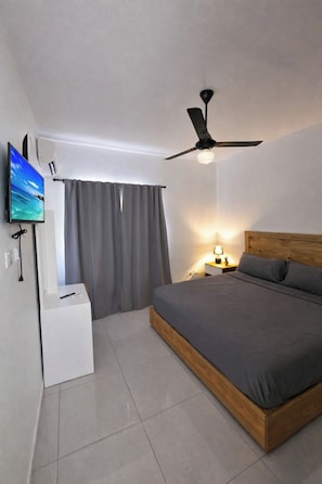 Ein modernes Schlafzimmer mit Bett, Deckenventilator, Fernseher und Nachttisch mit Lampe.
