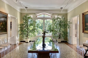 A spacious room with a large table, potted plants, and a view through a large window.
