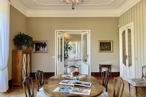 Ein Esszimmer mit rundem Tisch, Stühlen, einer Chandelierleuchtre und gerahmten Kunstwerken an den Wänden.