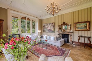 Ein geräumiges Wohnzimmer mit Kamin, einer Chandelier und einem großen Fenster mit Blick auf Grünflächen.