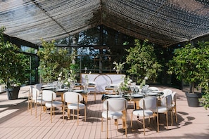 An outdoor dining area with round tables, white chairs, and potted plants.