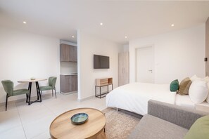 A modern hotel room with a bed, a sofa, a dining table, and a TV mounted on the wall. - Executive Suite with Balcony at The Bantree (Accra)