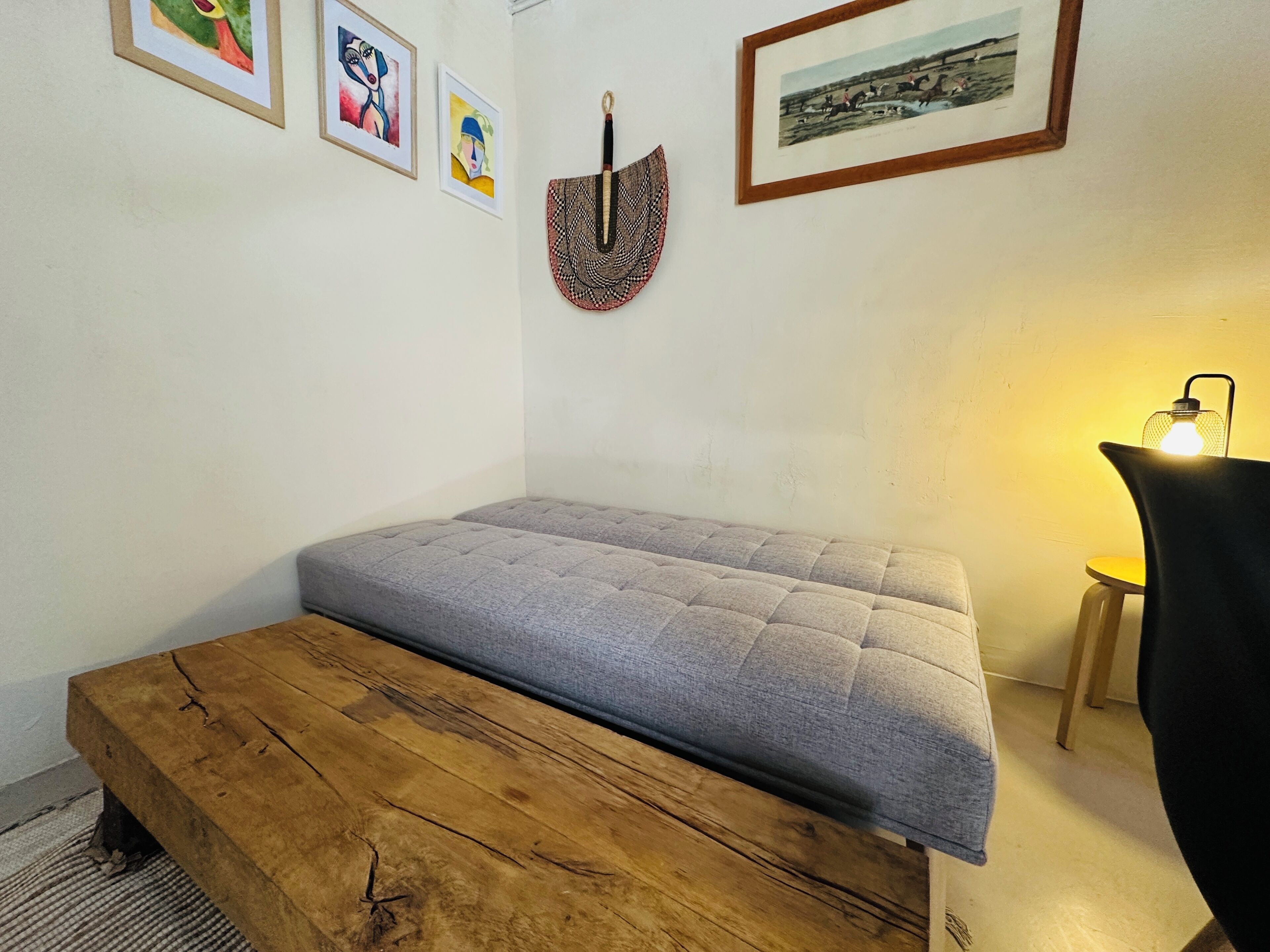 Ein Zimmer mit einem Bett, einer hölzernen Bank, einer Lampe und gerahmten Kunstwerken an der Wand.