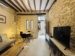 Ein gemütliches Wohnzimmer mit einer Couch, einem Esstisch mit Stühlen, einem Fernseher auf einem Lowboard und einer Steinwand.