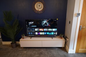 Een flatscreen televisie op een witte tv-meubel met een wandklok erboven.