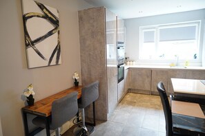 Een moderne keuken met een eethoek, inclusief een houten tafel, grijze stoelen en een groot abstract schilderij aan de muur.