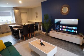 Een moderne woonkamer met een eethoek, een flatscreen televisie en een grote potplant.