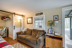 A cozy living room with a brown sofa, a wooden cabinet, a lamp, and a door leading to an outdoor area.