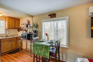 A kitchen with wooden cabinets, a dining table with chairs, a microwave, and a window with blinds.
