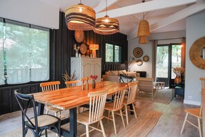 Un espace repas comprenant une table et des chaises en bois, un canapé et des luminaires suspendus en fibres tressées.