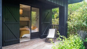 A wooden cabin with a bed, a chair, and a view of greenery. - La Petite Pinède : a peaceful villa between pines and a pond - La Pointe aux Chevaux (Lège-Cap-Ferret)