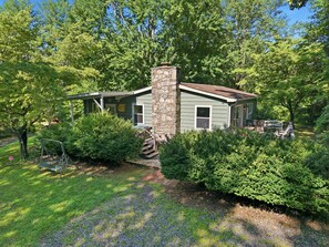 A small, single-story house with a stone chimney, surrounded by lush greenery and trees. - Whittier Cabin Retreat for Large Groups (Whittier)