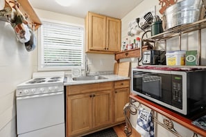 A compact kitchen with a stove, microwave, and wooden cabinets.