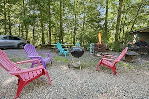 A campsite with outdoor seating, a barbecue grill, and a vehicle parked nearby.