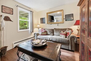 A living room with a sofa, a coffee table, a lamp, and a window with curtains. - Whittier Cabin Retreat for Large Groups (Whittier)