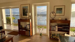 A spacious living room with large windows, a bookshelf, a desk, and a vase with flowers. - Waterfront 4* villa on the Etel ria. Ideal for families. (Plouhinec)