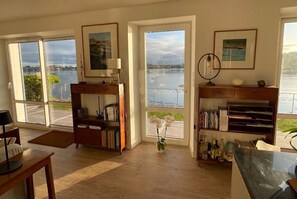 Un salón amplio con ventanas grandes, una estantería, un escritorio y un jarrón con flores.