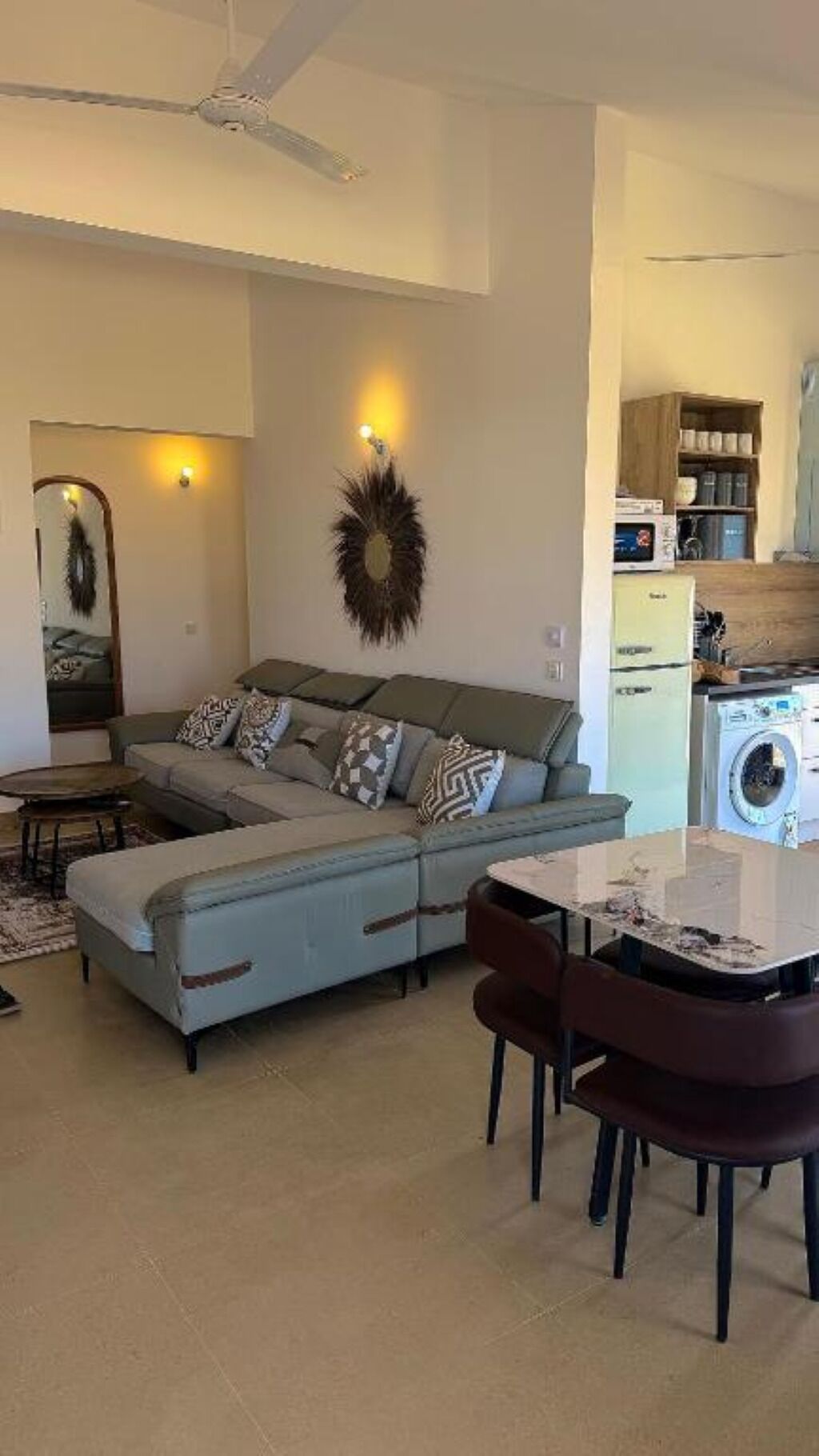 Een woonkamer met een bank, een eettafel met stoelen, een wasmachine en een keukenhoek.