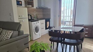 A compact living space with a sofa, dining table, chairs, a washing machine, and a potted plant. - 2-bedroom apartment in lovely Fumba Town with AC, modern comforts and balconies (Nyamanzi)