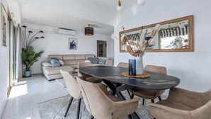 A modern living room with a round dining table, beige sofa, and a large mirror. - MC Riviera: Modern Apartment With Stunning sea View and Terrace Near Monaco (Beausoleil)