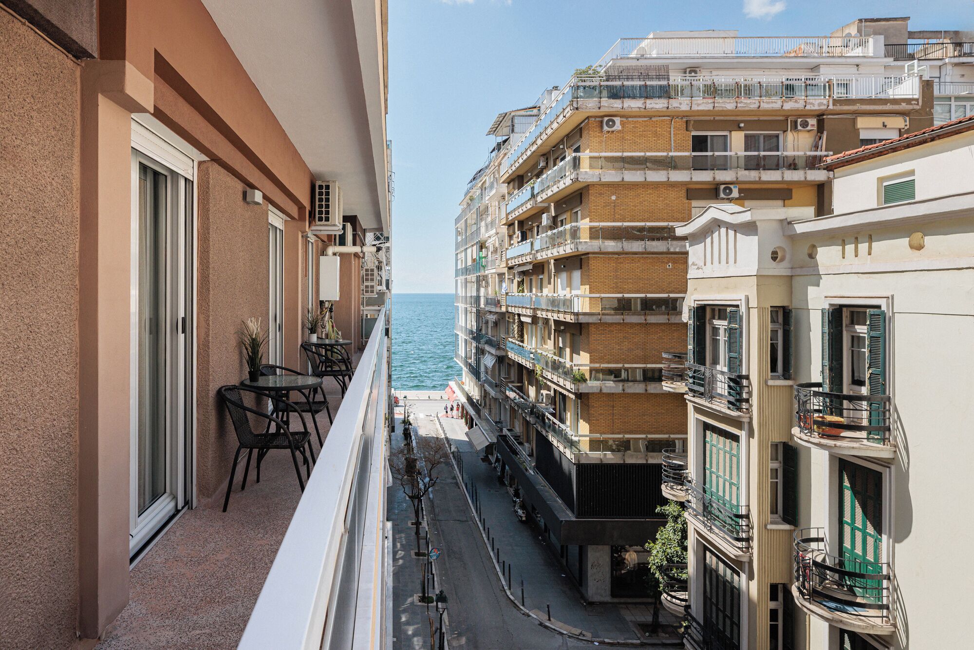 A balcony with a view of the sea, a street in the background, and a building with multiple balconies.