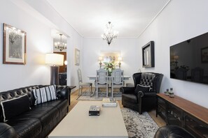 Un soggiorno con un divano in pelle nera, un tavolino da caffè, un tavolo da pranzo con sedie, un lampadario e opere d'arte incorniciate alle pareti.